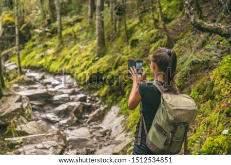 Hiker girl tourist taking picture with mobile phone of trail in nature forest hiking in Quebec outdoors fall autumn season, Canada travel lifestyle. Woman walking with backpack.