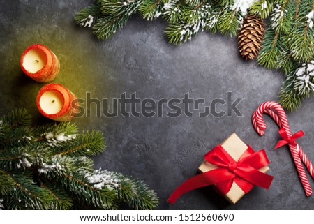 Christmas card with candles and fir tree branch covered by snow on stone background. Top view with space for your greetings