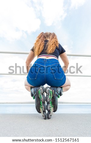 Back view of unrecognizable woman buttocks wearing short blue jeans shorts and roller skates enjoying her leisure time by the sea.