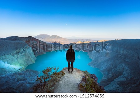 At sunrise girl stand on rock under volcano Kawah Ijen crater. Look at largest in world acid lake, sulphur mine. Popular travel destination, adventure hike on family vacation in Bali, Java, Indonesia Royalty-Free Stock Photo #1512574655