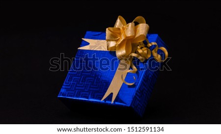 Close-up of Blue gift box decorated with golden ribbon isolated on black background