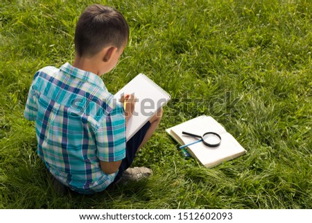 A boy holding a notebook and studying outside. The concept of homeschooling, 
search and discovery, science and knowledge in biology and botany, nature research. A child of Asian appearance. Image. Royalty-Free Stock Photo #1512602093