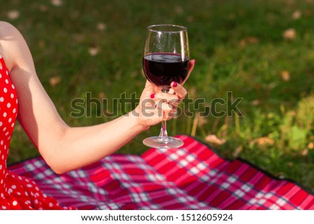 a glass of red wine in a female hand on the background of a lawn and captivity for a picnic