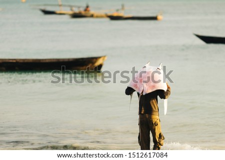 A fisherman is carrying a skate fish/stringray at Nungwi Beach / Zanzibar Royalty-Free Stock Photo #1512617084