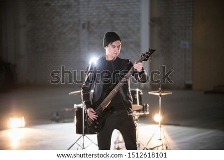 A musician man holding guitar and playing it on the background of a drum-kit