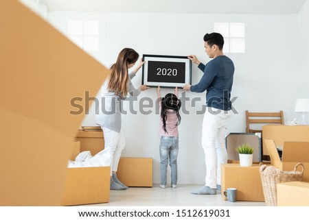Happy Asian family holding and putting picture frame on the wall. Young Man, Woman and little kid girl decorating room together. 2020 to 2021, New Year concept. Moving house. Royalty-Free Stock Photo #1512619031