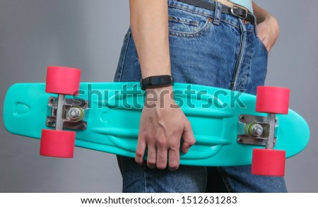 Young slim woman in jeans holds plastic skate board in her hands on a gray background. Youth hipster fashion. Crop photo