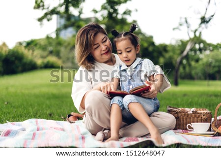 Portrait of happy grandmother and little cute girl enjoy relax reading a book together in summer park.Family and togetherness