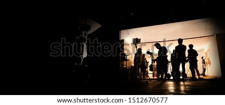 Silhoutte images of video production and lighting set for filming which movie crew team working and silhouette shadow of camera and professional equipment in big studio for commercial advertising. Royalty-Free Stock Photo #1512670577
