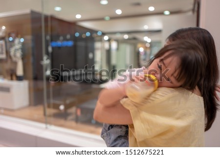 An Asian girl cried while sucking a bottle of milk in her mother's arms.