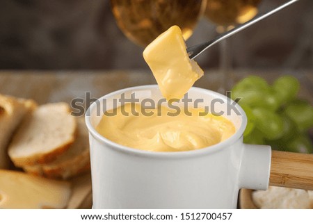 Dipping piece of cheese into tasty cheese fondue on table, closeup view