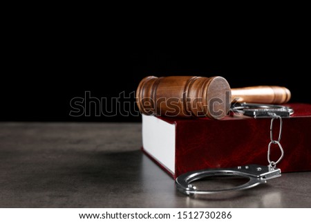 Judge's gavel, handcuffs and book on grey table against black background, space for text. Criminal law concept