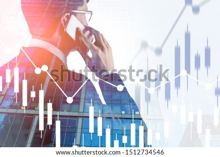 Handsome young businessman talking on smartphone in modern city with double exposure of graphs. Concept of business lifestyle and trading. Toned image