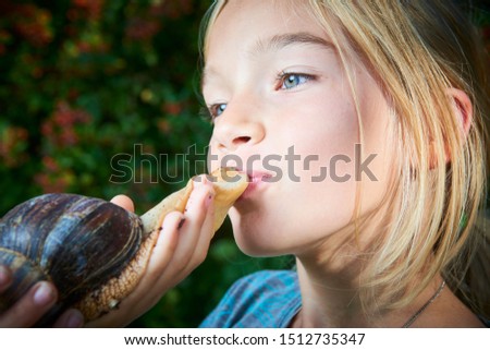 Portrait of preteen adorable child girl playing with her pet giant African snail (Achatina fulica). Kissing snail. Concept of not to be afraid of unusual animals. Selective focus