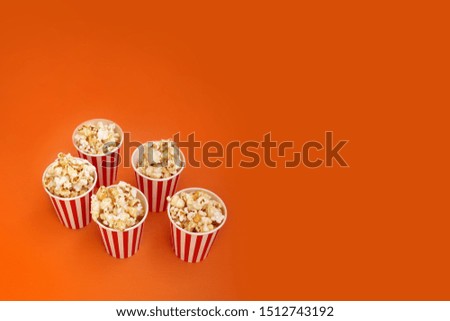 five striped red, white paper cups with popcorn in a row on a bright orange background, close-up, copy space, fast food concept