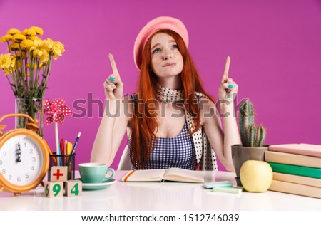 Photo of displeased student girl pointing fingers upward at copyspace while doing homework isolated over purple background