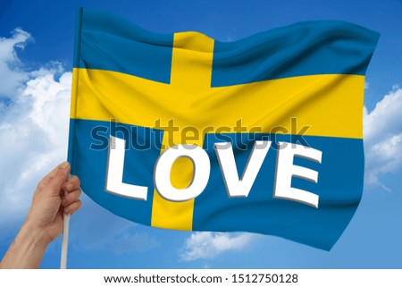 hand holds against the background of the sky with clouds the colored flag of Sweden on a luxurious texture of satin, silk with waves, closeup, copy space