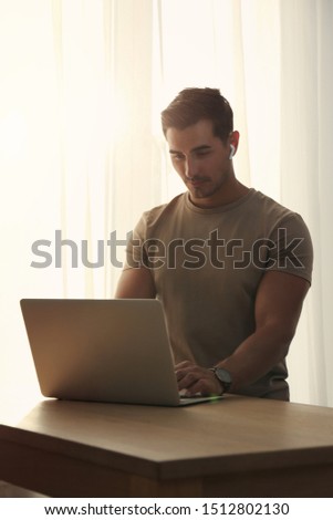 Portrait of young man with laptop at table indoors