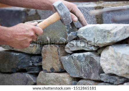 Close-up shot of a stonemason building a dry stone wall. Royalty-Free Stock Photo #1512865181