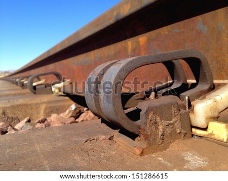 Looking down the side of train tracks brackets tapering into the distance with beautiful blue skies.