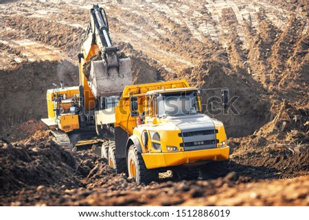 Loader excavator during earthmoving works loads soil ground into large yellow dump truck. Concept open mine. Royalty-Free Stock Photo #1512886019