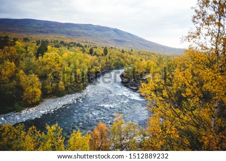 Sunny fall autumn view of Abisko National Park, Kiruna Municipality, Lapland, Norrbotten County, Sweden, with Abiskojokk river, road and Nuolja mountain, near border of Finland, Sweden and Norway Royalty-Free Stock Photo #1512889232