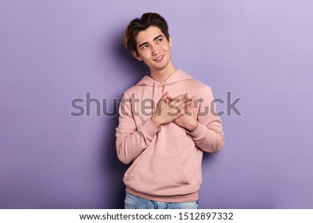young romantic attractive man looking up, keeping palms on heart. close up photo. isolated blue background, studio shot . copy space