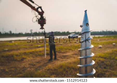 technician installing ground screw for mounting structure of solar panel at solar farm