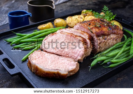 Traditional roasted dry aged veal tenderloin with beans and potatoes offered as closeup on a modern design cast iron tray  Royalty-Free Stock Photo #1512917273