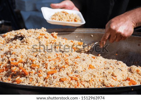 Real traditional street pilaf or plov, rice dish cooking in stock or broth, adding spices, and other ingredients such as vegetables or meat