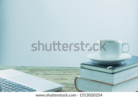 A white cup of coffee placed on the books with laptop computer on an old wooden table