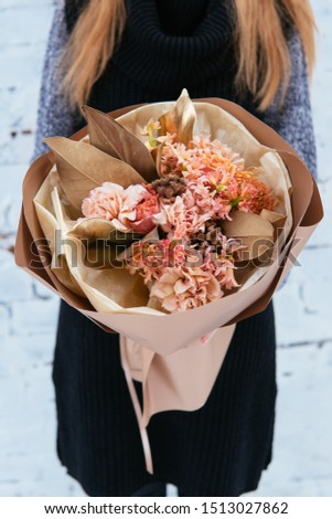 Bouquet of flowers in peach package in hands of woman florist in knitted sweater on background white brick wall.