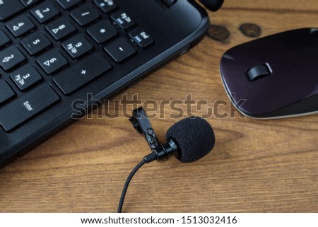 Lapel microphone with laptop and mouse on a wooden table.