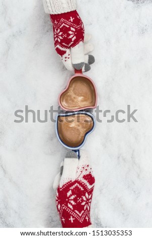 Male and female hands in Christmas gloves holding two cup of coffee in the heart form in the snow. New Year Christmas and winter concept. Instagram style