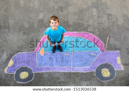 Adorable little kid boy playing with colorful chalks and painting big car picture on asphalt. Happy kid playing outside. Creative leisure for children outdoors in summer