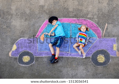 Two little children, kid boy and toddler girl having fun with with car picture drawing with colorful chalks on asphalt. Siblings painting on ground and playing together. Creative leisure for children