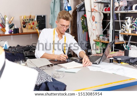 Confident  male  tailor using laptop and graphics tablet for creating pattern at sewing atelier