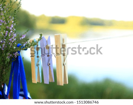 Pictures from a country holiday concept. Colored clothespins and a bunch of heather hanging on a clothesline. Blurred background of the lake and forest lit by the sun. Place for text.