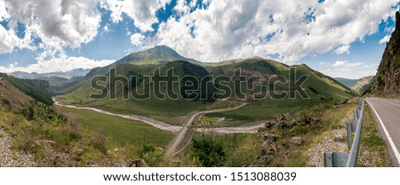 The road running in the mountains of the North Caucasus against the blue sky with clouds on a summer day