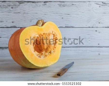 A large ripe pumpkin is cut with a knife on a white wooden background.