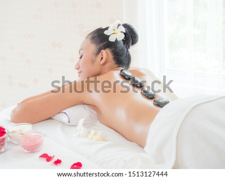 A beautiful Asian woman is relaxing in a spa shop when an expert masseuse places a hot stone on her back