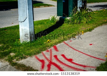 Pattern of hydro line markings on a sidewalk next to a metal street light pole and transformer,