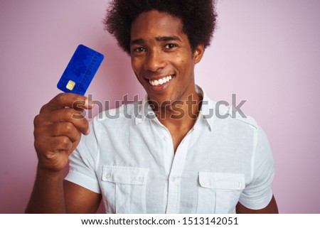 Afro american customer man holding credit card standing over isolated pink background with a happy face standing and smiling with a confident smile showing teeth
