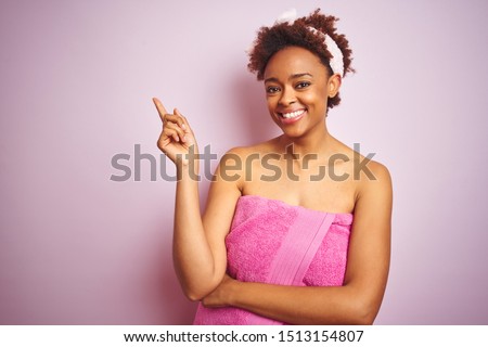 African american woman wearing shower towel after bath over pink isolated background with a big smile on face, pointing with hand and finger to the side looking at the camera.
