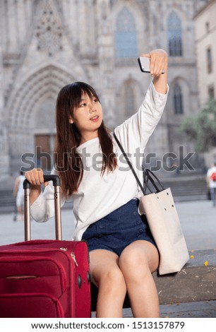 Attractive young chinese woman sits on stone staircase and makes selfies against the background of sights