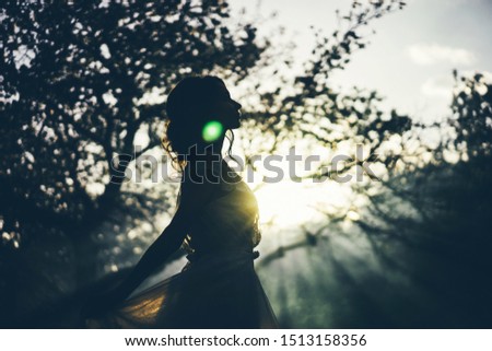 Silhouette of young beautiful woman in white dress in blooming garden with magic light. Bride.