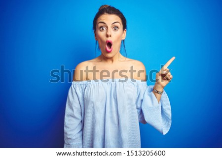 Young beautiful woman wearing bun hairstyle over blue isolated background Surprised pointing with finger to the side, open mouth amazed expression.