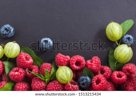 Frame made of different berries, raspberries, blueberries, gooseberries and mint on black background