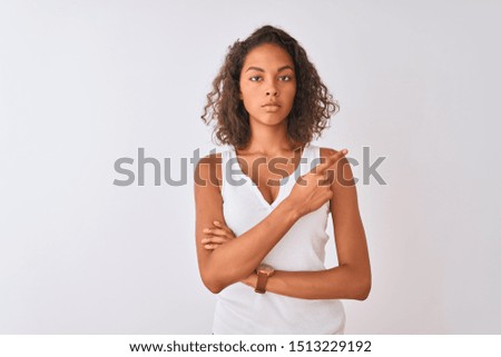 Young brazilian woman wearing casual t-shirt standing over isolated white background Pointing with hand finger to the side showing advertisement, serious and calm face
