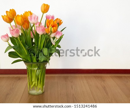 Bouquet of pink and orange tulips in the vase is on the wood floor and white wall background